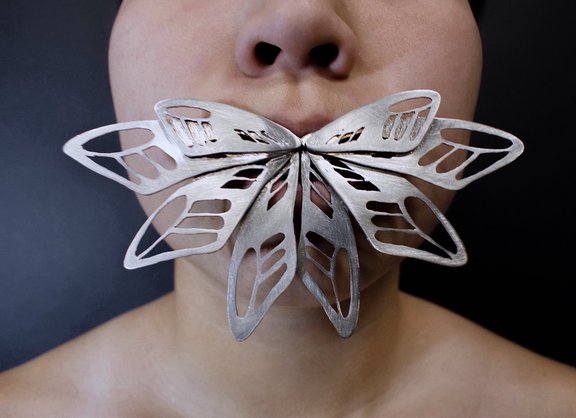 Metal cut-out butterfly wings held in mouth.